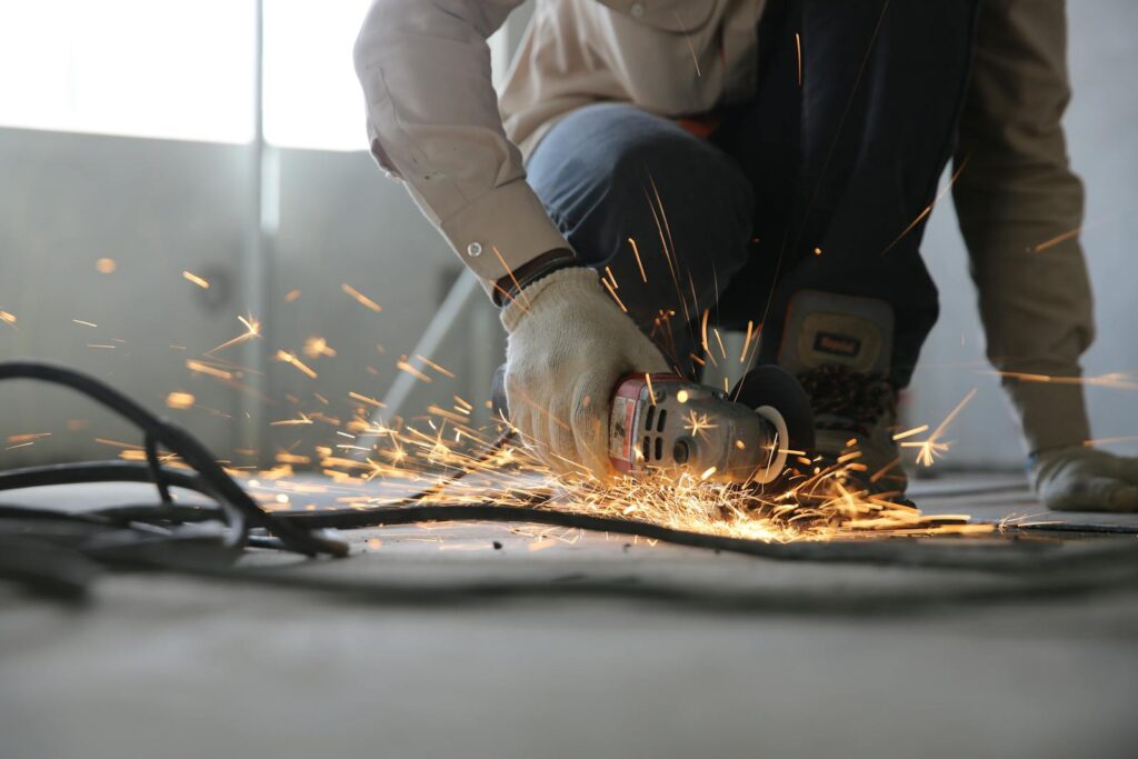 Salvador Construcciones Huelva A skilled industrial worker uses a grinder creating a burst of sparks indoors.